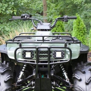 Op de afbeelding: Een groene ATV met een zwarte rolkooi en zwarte wielen. De ATV staat op een grasveld. De ATV heeft twee koplampen en een zwarte bumper.
