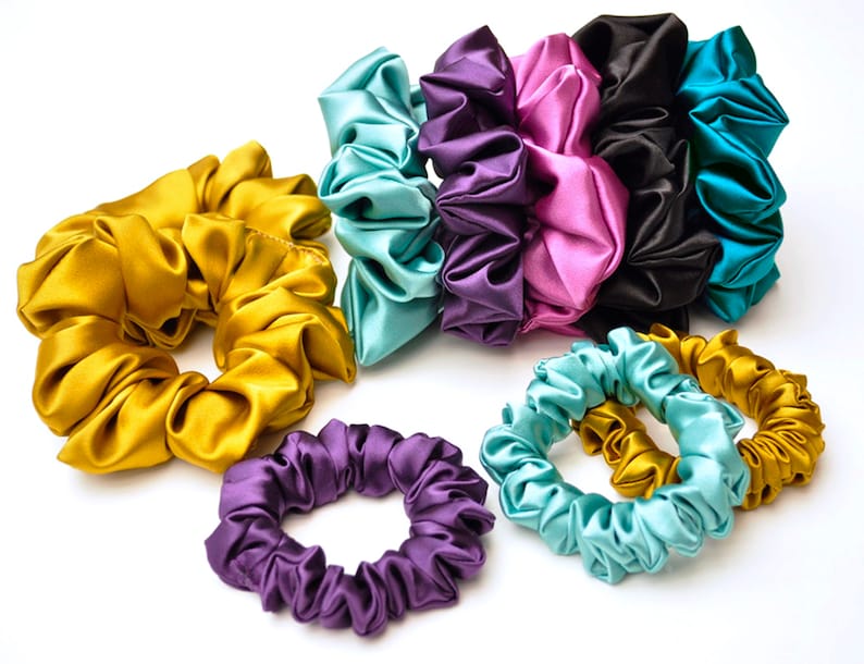 May include: A set of colorful satin scrunchies in various shades of teal, purple, pink, gold, and black. The scrunchies are made of soft, silky fabric and are perfect for holding hair in place.