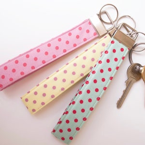 May include: Three fabric keychains with polka dot patterns in pink, yellow, and green. The keychains are attached to silver key rings with two keys.