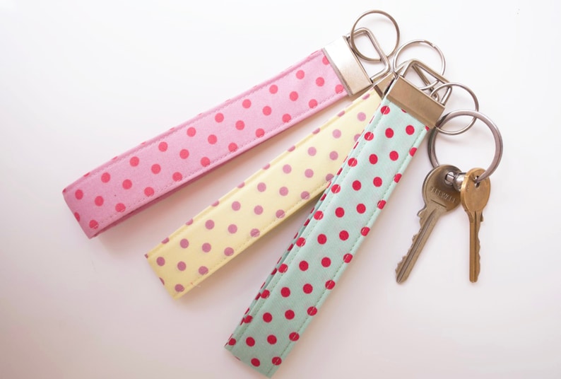May include: Three fabric keychains with polka dot patterns in pink, yellow, and green. The keychains are attached to silver key rings with two keys.