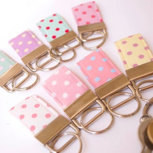 May include: A set of eight keychains with different colored polka dot fabric. Each keychain has a silver metal ring and a silver metal clasp.