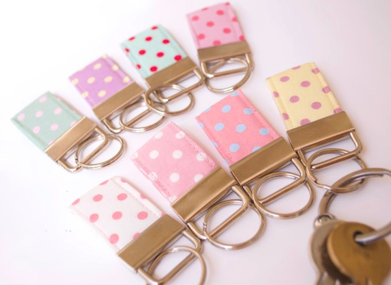 May include: A set of eight keychains with different colored polka dot fabric. Each keychain has a silver metal ring and a silver metal clasp.