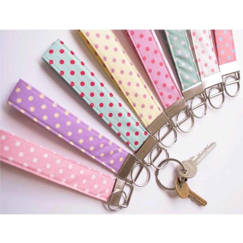 May include: A set of eight colorful keychains with polka dot patterns. Each keychain has a silver key ring and is made of fabric.
