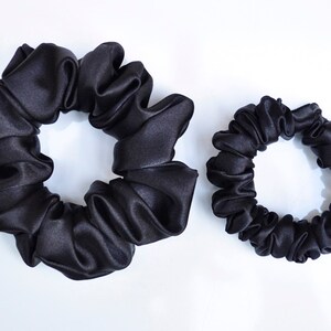 May include: Two black satin scrunchies, one larger than the other. The scrunchies are made of soft, silky fabric and are designed to be gentle on hair.