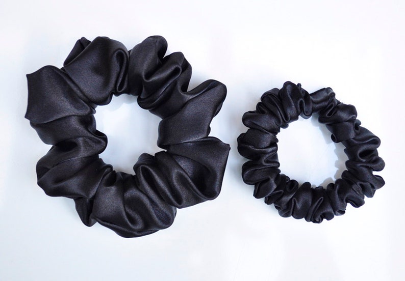 May include: Two black satin scrunchies, one larger than the other. The scrunchies are made of soft, silky fabric and are designed to be gentle on hair.