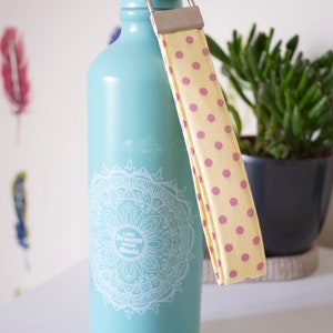 May include: A turquoise water bottle with a white mandala design and the text "Less Dreams More Goals". The bottle has a yellow and pink polka dot strap.
