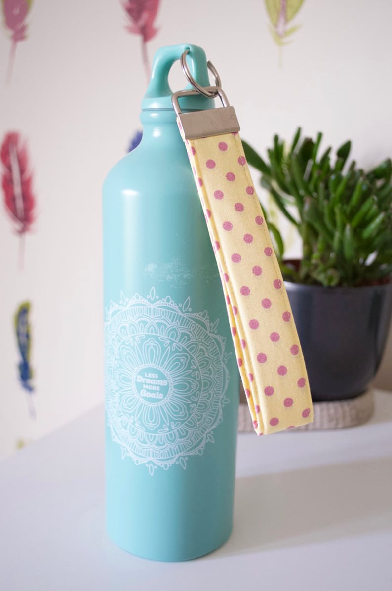 May include: A turquoise water bottle with a white mandala design and the text "Less Dreams More Goals". The bottle has a yellow and pink polka dot strap.