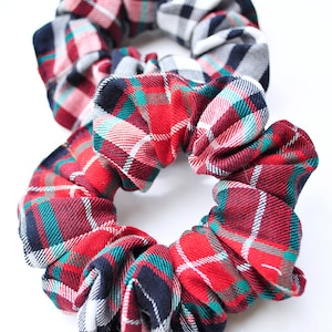 May include: Two red, white and green plaid scrunchies. The scrunchies are made of fabric and have a gathered look.