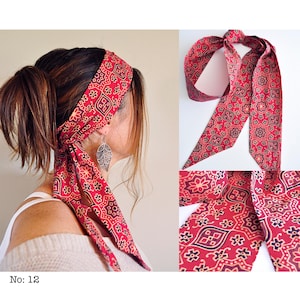 May include: Red patterned headband with a matching scarf. The fabric features a repeating floral and geometric design in red, black, and beige. The headband is tied around the head with the scarf hanging down. The text "No: 12" is visible.