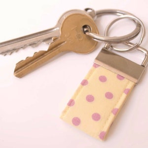 May include: A yellow and pink polka dot fabric keychain with a silver metal key ring and two keys attached.