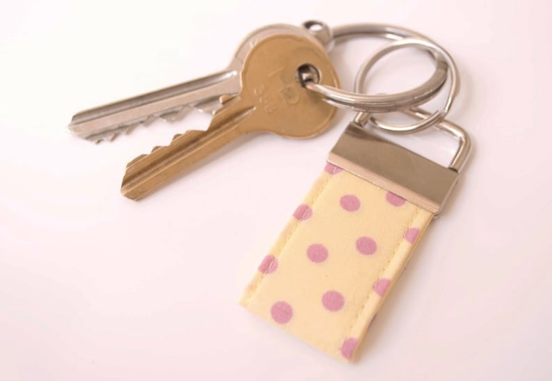 May include: A yellow and pink polka dot fabric keychain with a silver metal key ring and two keys attached.