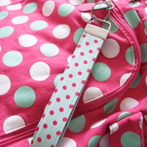 May include: A pink polka dot bag with a light blue and white polka dot key chain. The bag has a zipper closure and a strap.