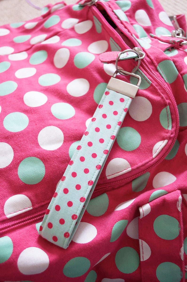 May include: A pink polka dot bag with a light blue and white polka dot key chain. The bag has a zipper closure and a strap.