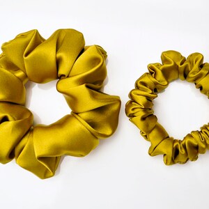 May include: Two gold satin scrunchies, one larger and one smaller, on a white background.