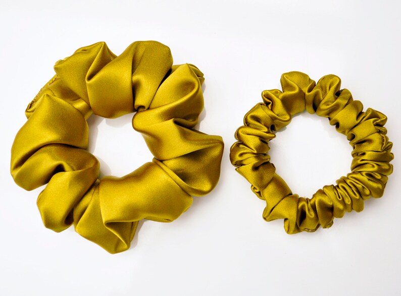 May include: Two gold satin scrunchies, one larger and one smaller, on a white background.