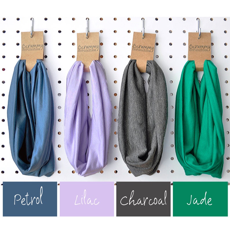 May include: Four fabric headbands in petrol blue, lilac, charcoal grey, and jade green, displayed on a pegboard. Each headband has a brown tag with the text "Scrummy Scrunchies". Below each headband is a colour-matched label with the colour name.