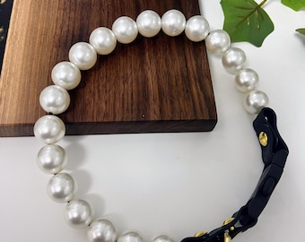 May include: A white pearl dog collar with a black leather strap and gold clasp.