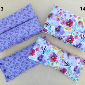 May include: Four rectangular fabric items, two with a lavender floral pattern and two with a vibrant floral design in pink, purple, and yellow. The lavender items have a button closure. The items are likely fabric pouches or cases.