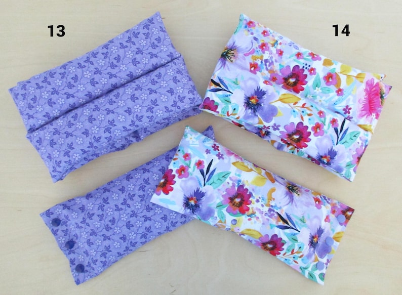 May include: Four rectangular fabric items, two with a lavender floral pattern and two with a vibrant floral design in pink, purple, and yellow. The lavender items have a button closure. The items are likely fabric pouches or cases.