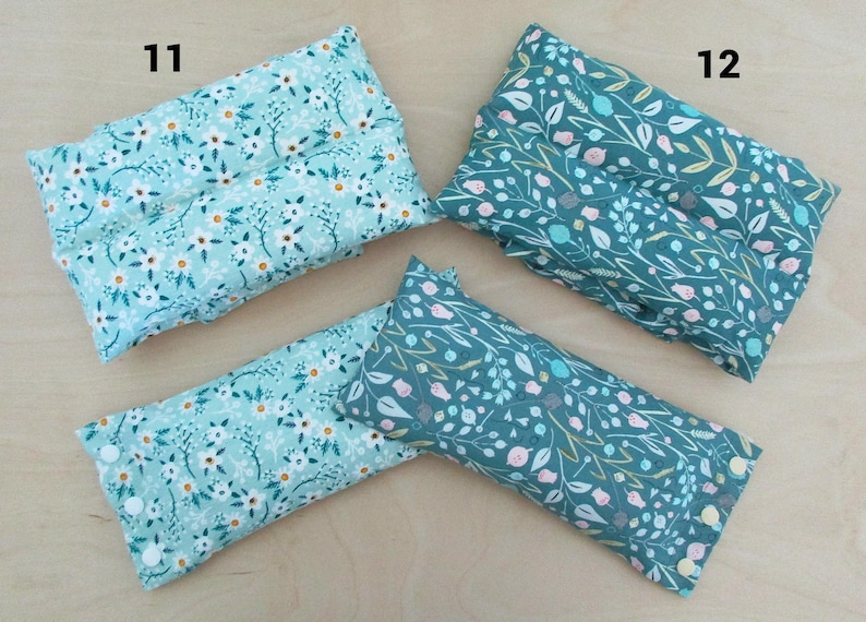 May include: Four rectangular fabric items with floral patterns. Two are light blue with white flowers, and two are teal with white, pink, and yellow floral designs. The items are arranged on a light wood surface. Numbers 11 and 12 are visible.