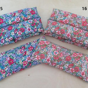 May include: Three floral fabric items, two rectangular and one V-shaped, are displayed. The fabrics feature a pattern of small red, pink, blue, and purple flowers on a light background. The V-shaped item has buttons on the ends.