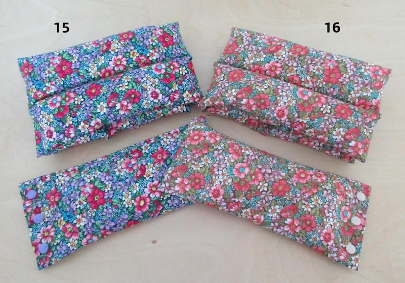 May include: Three floral fabric items, two rectangular and one V-shaped, are displayed. The fabrics feature a pattern of small red, pink, blue, and purple flowers on a light background. The V-shaped item has buttons on the ends.