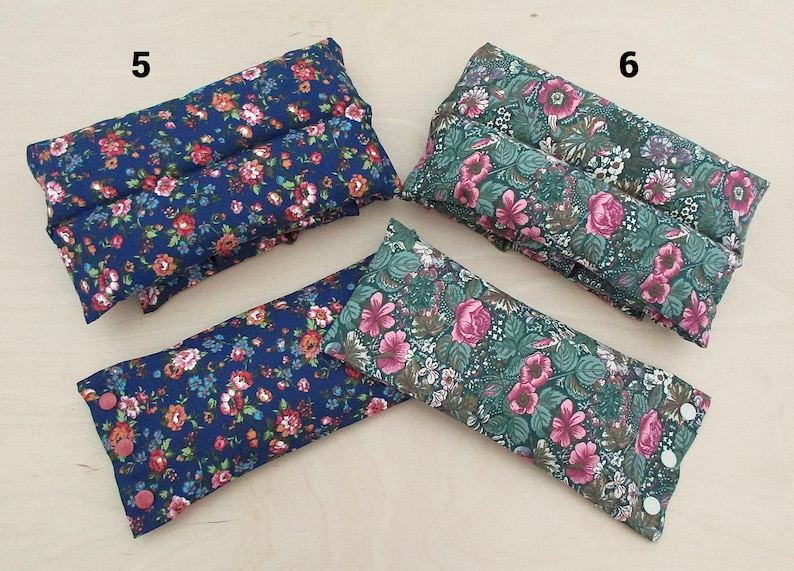 May include: Several rectangular, floral-patterned pillows in shades of blue and green. The pillows feature a variety of colorful flowers. Some pillows have button closures. The pillows are likely for relaxation or therapeutic use.