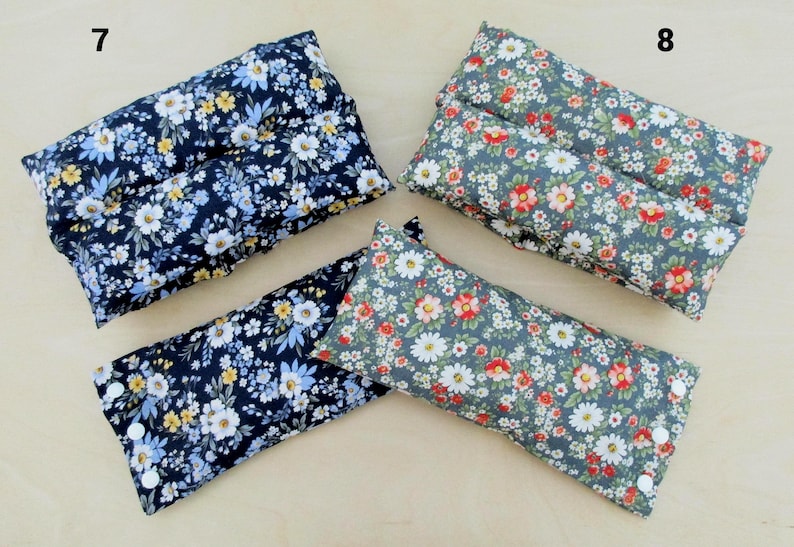 May include: Rectangular floral print pillows in navy blue and gray. The navy pillows feature white, yellow, and blue flowers. The gray pillows have red, white, and pink flowers. Each pillow has a button closure on one end.