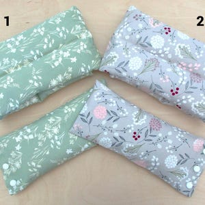 May include: Four rectangular, floral-patterned pillows. Two are sage green with white flowers, and two are gray with pink and white flowers. Each pillow has a button closure on one end.