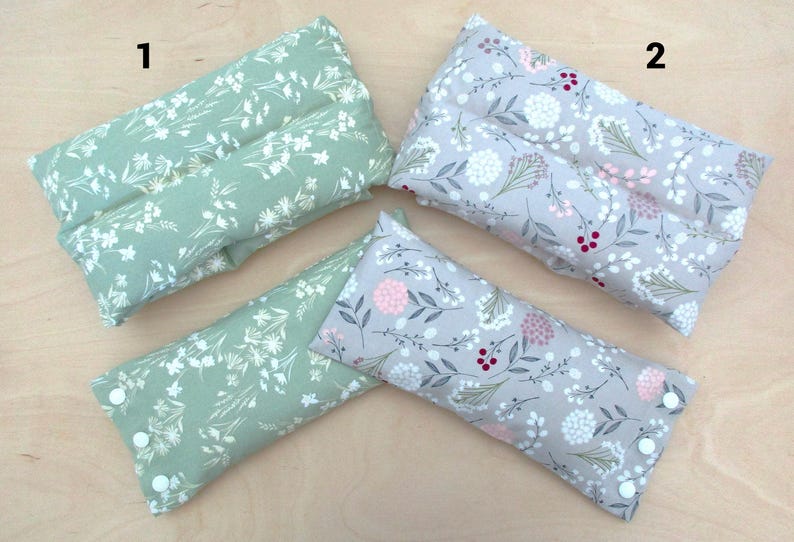 May include: Four rectangular, floral-patterned pillows. Two are sage green with white flowers, and two are gray with pink and white flowers. Each pillow has a button closure on one end.