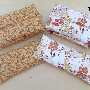 May include: Four rectangular fabric items with floral and leaf patterns. Two are yellow with red and green leaves, and two are white with red, brown, and yellow flowers. One yellow item has buttons.