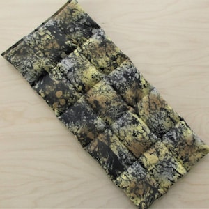 May include: A rectangular, quilted heating pad with a marbled pattern in black, gold, and silver. The pad is divided into rectangular sections. The fabric has a mottled appearance, with the colors blending together.