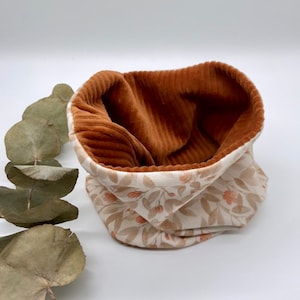 May include: A brown corduroy fabric neck warmer with a white floral print lining. The neck warmer is folded and displayed on a white surface.
