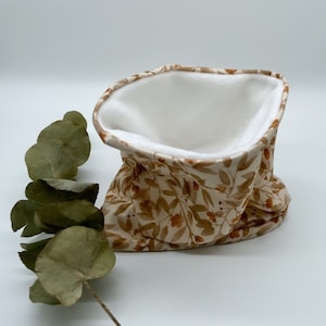 May include: A beige neck warmer with a floral pattern and a white fleece lining. The neck warmer is folded and displayed on a white surface.