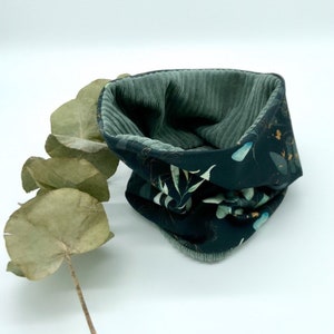 Op de afbeelding: Een donkergroene en zwarte nekwarmer met een bloemenpatroon. De nekwarmer is gemaakt van een zachte, comfortabele stof en heeft een geribbelde textuur.
