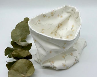 May include: A white fabric cowl scarf with a floral pattern. The scarf is folded, revealing a contrasting floral interior. Dried eucalyptus leaves are on the left side of the image. The scarf is made of soft fabric.