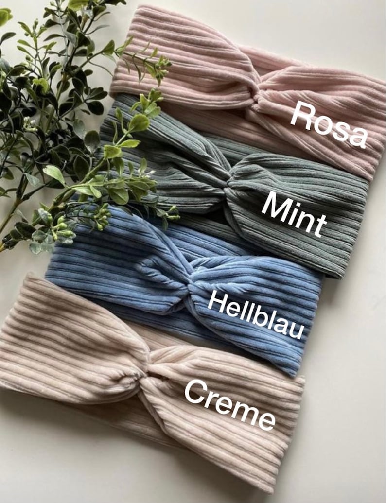 May include: Four fabric headbands in different colors: cream, light blue, mint green, and pink. Each headband has a knotted design and is labeled with its color name in German.