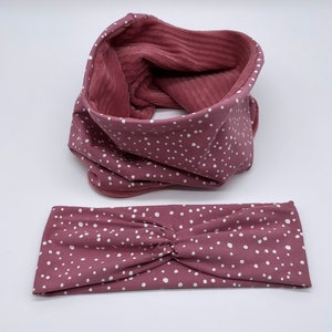 Può includere: Un cerchietto e un scaldacollo abbinati a pois bianchi su sfondo rosa. Il cerchietto è attorcigliato e lo scaldacollo è piegato.