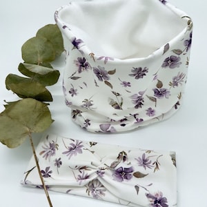 Puede incluir: Un conjunto de diadema y cuello de cuello blanco con un patrón floral morado. La diadema está retorcida y el cuello de cuello está doblado.