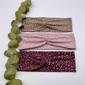 May include: Three fabric headbands with a white polka dot pattern on a brown, pink, and burgundy background.