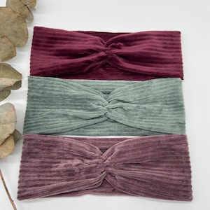 May include: Three velvet headbands in burgundy, sage green, and mauve. The headbands are ribbed and have a twisted knot in the centre.