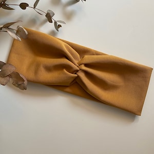 Könnte beinhalten: Ein gelbes Stoff Stirnband mit einem Knotendetail. Das Stirnband ist aus weichem, dehnbarem Material.