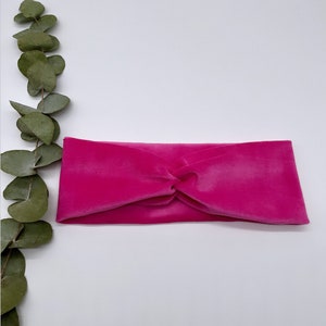 May include: A bright pink velvet headband with a knotted design. The headband is on a white background.