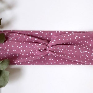 Könnte beinhalten: Ein rosa Stirnband mit weißen Punkten. Das Stirnband ist aus weichem, dehnbarem Stoff gefertigt und so konzipiert, dass es bequem zu tragen ist.