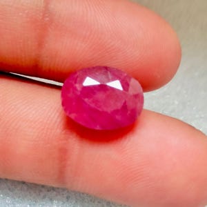Puede incluir: Una piedra preciosa de rubí ovalada de color rosa vibrante con un corte facetado.