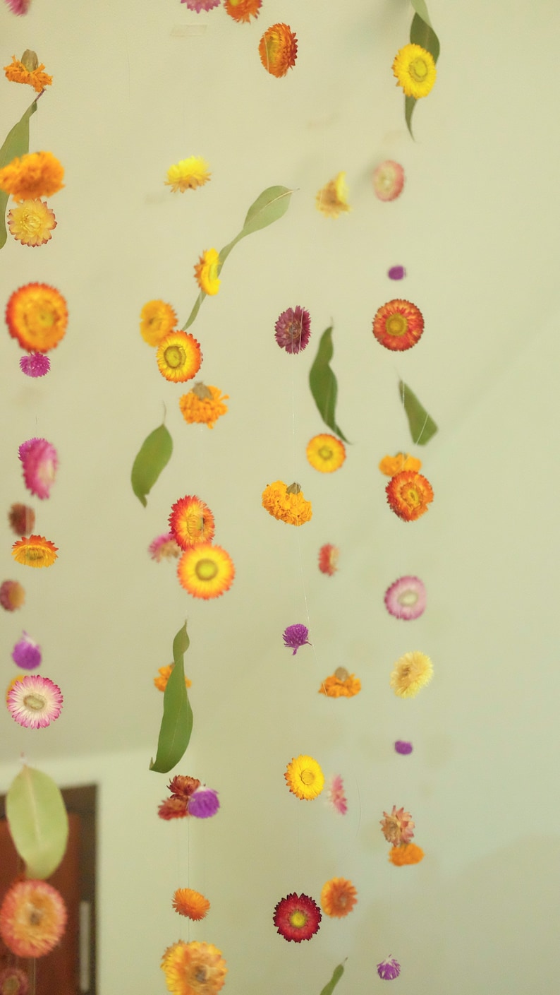 Peut inclure: Un mobile de fleurs color&eacute; avec des fleurs s&eacute;ch&eacute;es dans des tons de jaune, orange, rose et violet suspendu &agrave; un plafond blanc.