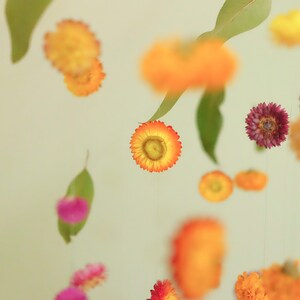 Peut inclure: Un mobile compos&eacute; de fleurs et de feuilles s&eacute;ch&eacute;es. Les fleurs sont dans des tons d'orange, jaune, rose et violet. Les feuilles sont vertes. Le mobile est suspendu &agrave; un plafond.