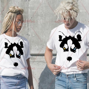 Könnte beinhalten: Zwei weiße T-Shirts mit einem schwarzen und weißen Wolfskopf-Motiv. Der Wolf hat ein gelbes Auge und ein blaues Auge.