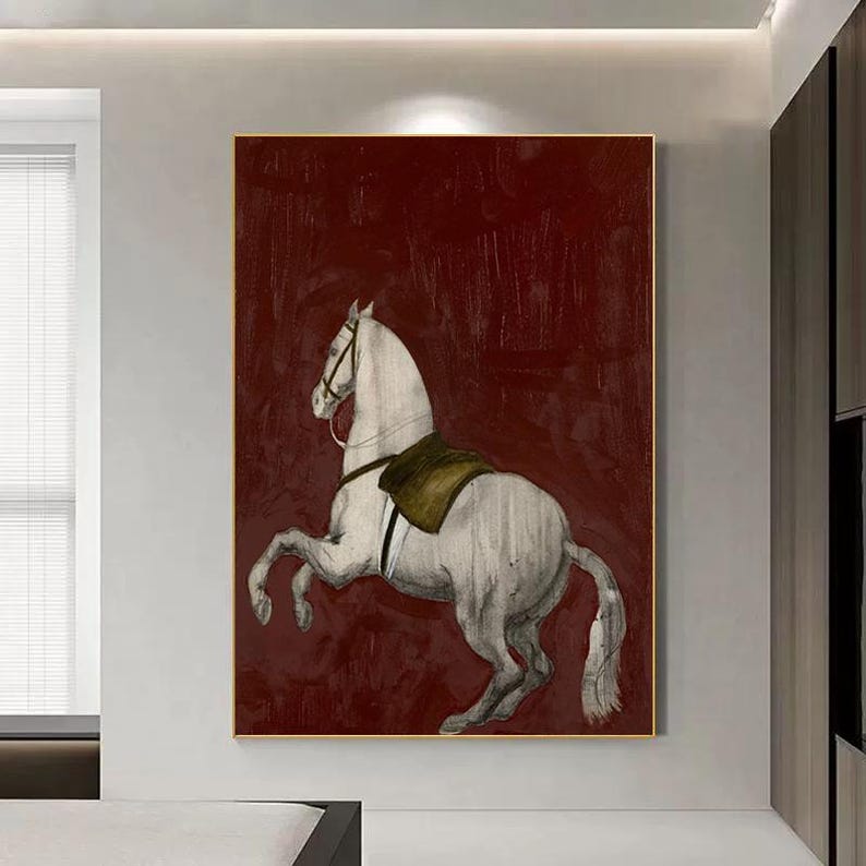 May include: A framed artwork featuring a white horse rearing up against a deep red background. The horse has a saddle and bridle, and the artwork is in a gold frame. The style is reminiscent of a classic equestrian painting.