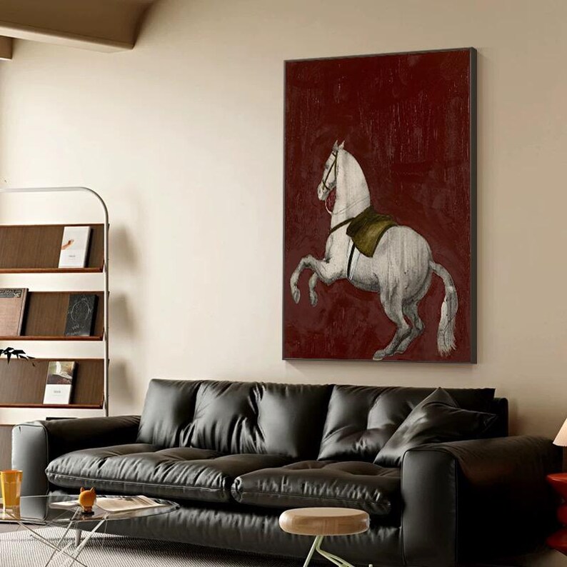 May include: A framed canvas art print featuring a white horse rearing up against a deep red background. The horse has a saddle and bridle, and the artwork has a vintage, textured appearance. The artwork is displayed above a black leather sofa.